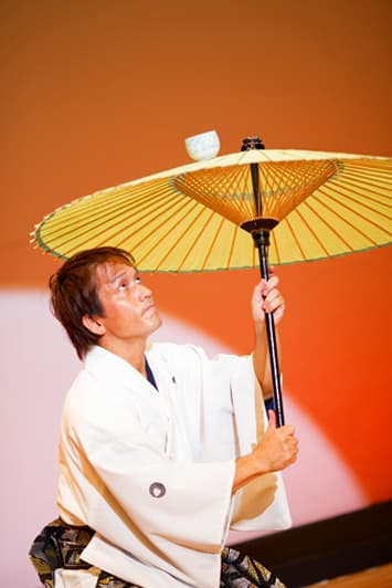 開いた和傘の上で湯呑茶碗を回す様子