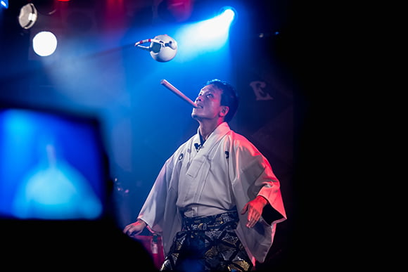 ステージに立ち口にくわえたバチで土瓶を操る豊来家幸輝